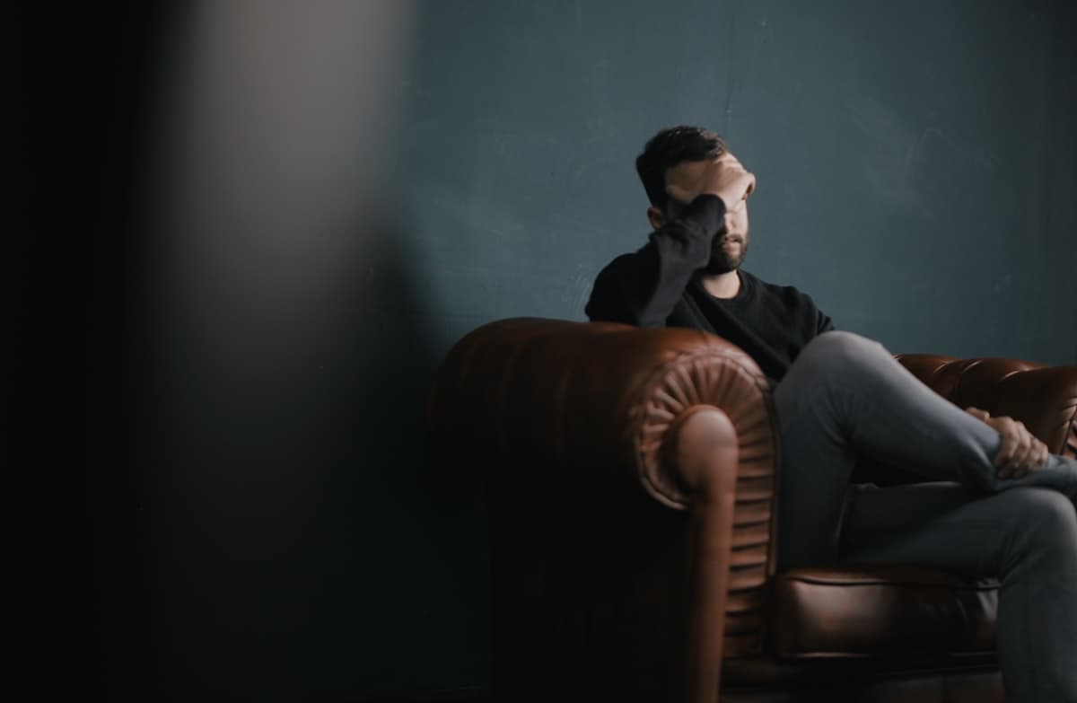 Man sitting alone on a sofa with his head in his hand, appearing distressed